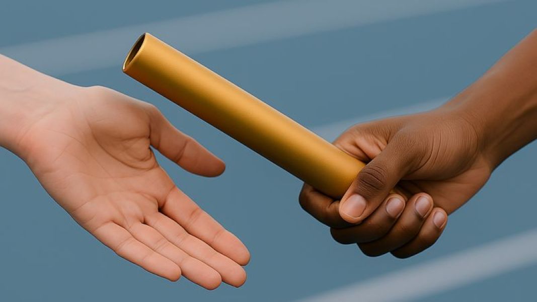Close-up of two hands passing a gold relay baton; one hand is reaching out to receive it, whilst the other hand is holding it against a blurred blue background, likely a running track.